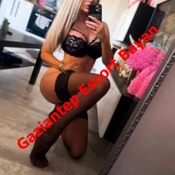 Woman in black lace lingerie posing on her knees in a bedroom, taking a mirror selfie; red text advertises Gaziantep Escort Bayan.