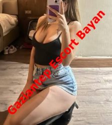 Mirror selfie of a woman wearing a black tank top and denim shorts, kneeling on a stool in a room, with bold red diagonal text reading 'Gaziantep Escort Bayan' across the image.